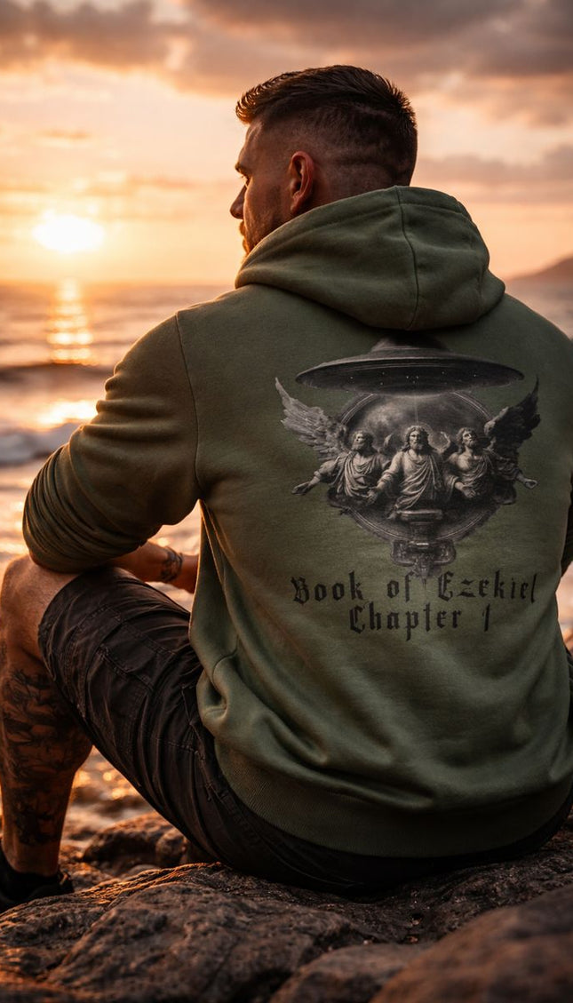 Man wearing a green hoodie with a graphic design sitting on a rocky beach at sunset.
