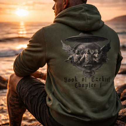 Man wearing a green hoodie with a graphic design sitting on a rocky beach at sunset.